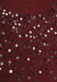 Pull en maille bordeaux avec des paillettes argentées et noires dispersées sur le devant, créant un effet texturé et scintillant.