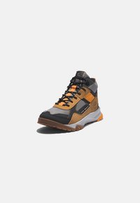Chaussure de randonnée montante en gris, noir et orange avec semelle robuste, panneaux en mesh et fermeture à lacets sur fond blanc.