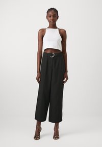 Top corto bianco, pantaloni neri a gamba larga con una fibbia argentata, e sandali con tacco. Tessuto morbido, top aderente, fondo rilassato.