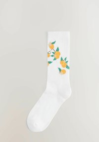 Hvide ribbede sokker med et mønster af gule appelsiner med grønne blade. Designet er vævet ind i stoffet og viser klare farver.