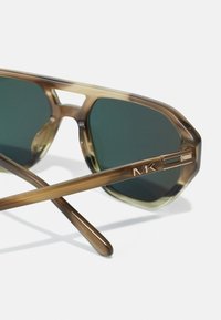 Ochelari de soare cu ramă octagonală, model din scoică brună, lentile verzi și logo MK auriu pe braț. Unghiurile lentilelor și ale brațelor sunt vizibile.