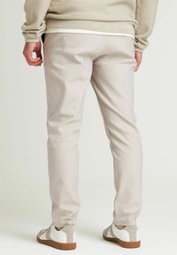 Lichtbeige taps toelopende broek van zachte stof, met een gladde afwerking en een elastische tailleband, gecombineerd met wit en grijs schoeisel.