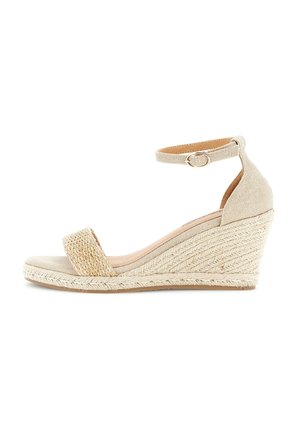 Beige kile-sandal med vævet frontrem, ankelrem med spænde og flettet espadrille-agtig hæl på hvid baggrund.