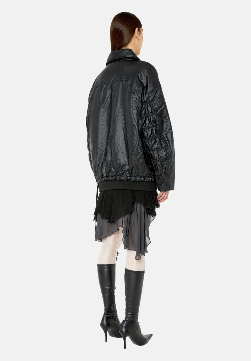 Schwarze Puffjacke mit gesteppten Ärmeln, elastischem Saum und Stehkragen. Getragen über einem schichtweisen, schwarz-grauen Kleid und knielangen schwarzen Stiefeln.