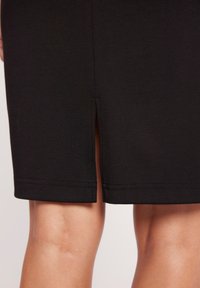 Czarna sukienka o długości do kolan, z bocznym rozcięciem, gładką teksturą i starannie wykończonym dołem.