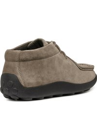 Zapatos de ante de color marrón claro con forma redondeada, altura baja en el tobillo, suela plana de goma negra y un patrón de textura visible en la suela. Diseño de cordones en la parte delantera.