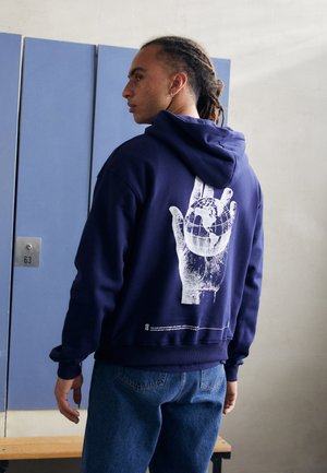 Navy blue hoodie with a large white graphic of a hand holding a globe on the back, featuring ribbed cuffs and waistband.