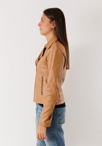 Giubbotto in pelle marrone con chiusura a zip, tasche laterali e spalline. Il design presenta una silhouette aderente e una texture liscia.