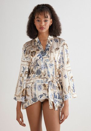 Jedwabny kimono w kolorze kremowym z niebieskimi i brązowymi kwiatowymi wzorami. Posiada fason z zamknięciem z przodu, rękawy dzwonowate i pasek w talii.