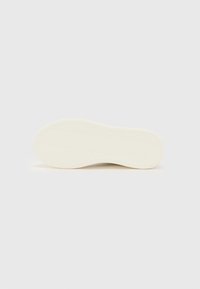 Semelle de sneaker plate en beige avec un motif en chevrons texturé et un bord lisse et arrondi. Design épuré sans logos ni embellissements visibles.
