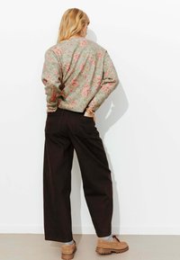 Pull en maille verte à motif floral, coupe ample, associé à un pantalon noir taille haute. La tenue est complétée par des chaussures marron à semelles texturées.