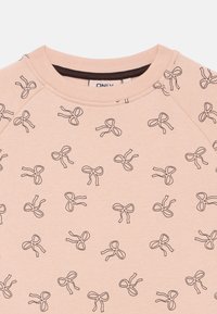 Gaiši rozā sporta krekls ar atkārtotu melnu loku rakstu, apaļu kakla izgriezumu un mīkstu tekstūru.