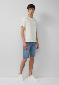 Witte T-shirt met korte mouwen, gecombineerd met lichtblauwe denim shorts en witte sneakers. Eenvoudig ontwerp met een casual pasvorm, zonder zichtbare patronen of accenten.