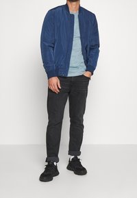 Chaqueta bomber de color marino con puños acanalados, combinada con una camiseta de color azul claro y jeans de color gris oscuro. Zapatillas deportivas negras completan el atuendo.