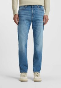 Blue denim jeans with a straight-leg cut, light wash, slight fading, five-pocket design, and contrasting stitching. Paired with beige sneakers.