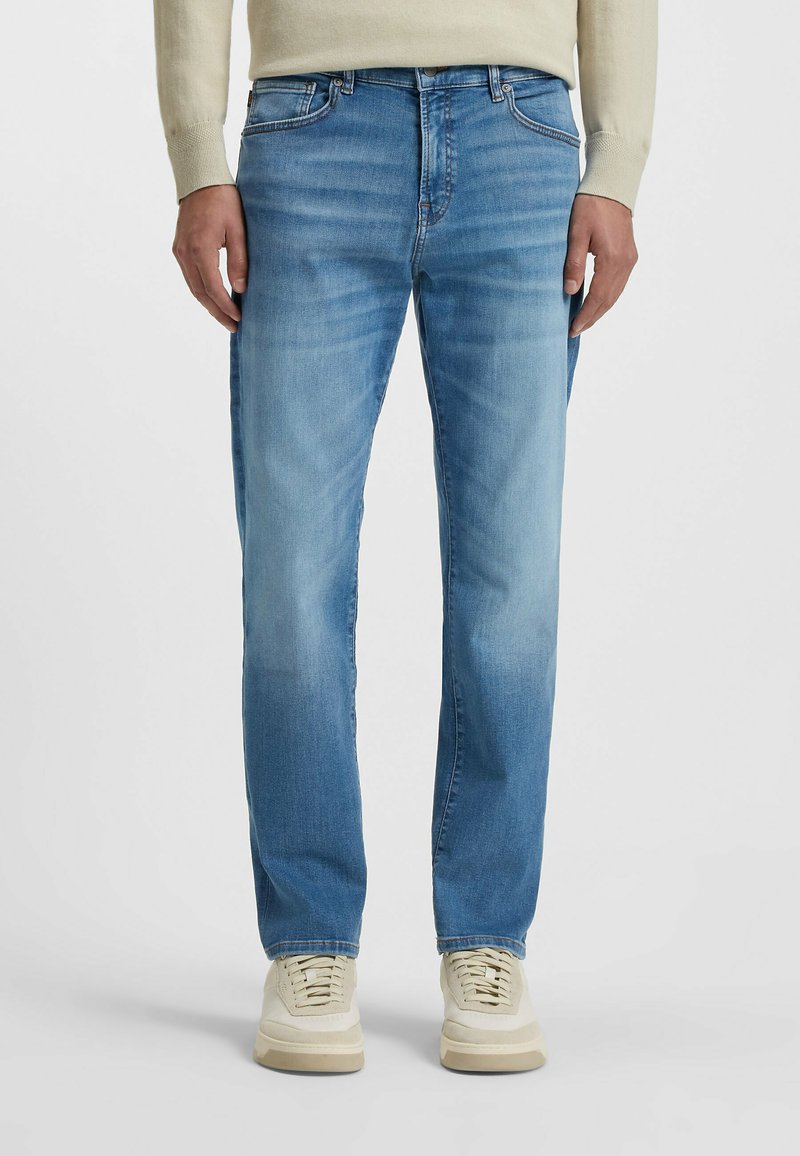 Blue denim jeans with a straight-leg cut, light wash, slight fading, five-pocket design, and contrasting stitching. Paired with beige sneakers.