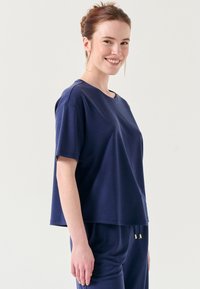 T-shirt a maniche corte blu navy con una vestibilità comoda, scollo rotondo e texture morbida. Abbinato a pantaloni coordinati con coulisse.