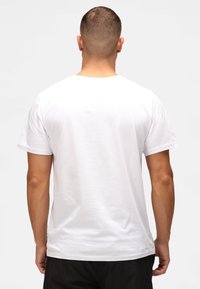 Valkoinen puuvillainen t-paita, jossa on pyöreä pääntie ja lyhyet hihat. Sujuva pinta, normaali mitoitus, eikä näkyviä logoja tai kuvioita selässä.