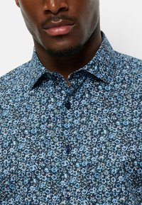 Blaues Blumen-Hemd mit Knöpfen, das ein blaues und weißes Blumenmuster zeigt, klassischen Kragen und dunklen Knöpfen. Aus Baumwolle, mit strukturiertem Finish.