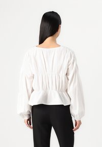 Blusa bianca a maniche a sbuffo con vita arricciata e polsini elasticizzati. Tessuto leggero con una texture liscia, che arriva sopra la vita.