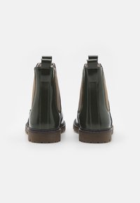 Botas Chelsea de charol verde con paneles laterales de ante marrón, gomas elásticas, tirador trasero y suela de goma texturizada.