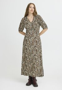 Robe maxi imprimé léopard avec de courtes manches bouffantes, décolleté en V, taille cintrée et fentes latérales ; le tissu a une texture lisse. Portée avec des bottes marron.
