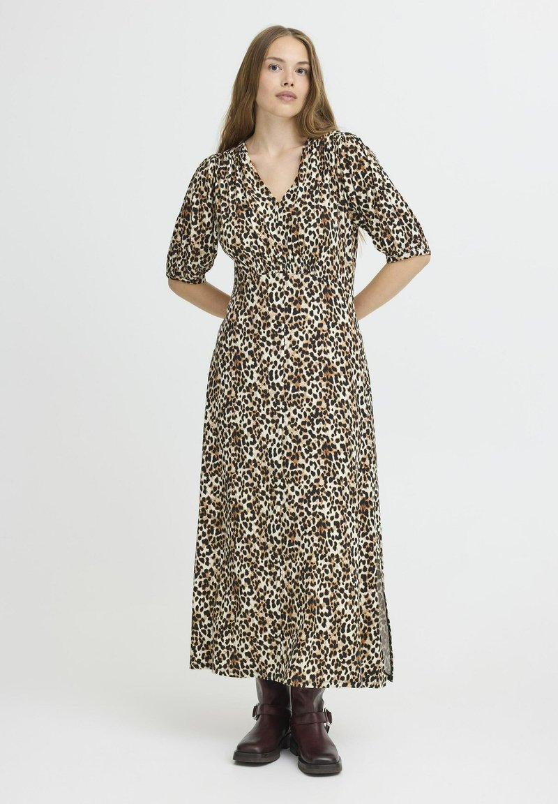 Robe maxi imprimé léopard avec de courtes manches bouffantes, décolleté en V, taille cintrée et fentes latérales ; le tissu a une texture lisse. Portée avec des bottes marron.