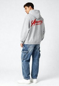 Grauer Sweatshirt mit "Amore" in roter Schreibschrift auf dem Rücken, kombiniert mit hellblauen Cargo-Jeans mit mehreren Taschen und weißen Sneakern.