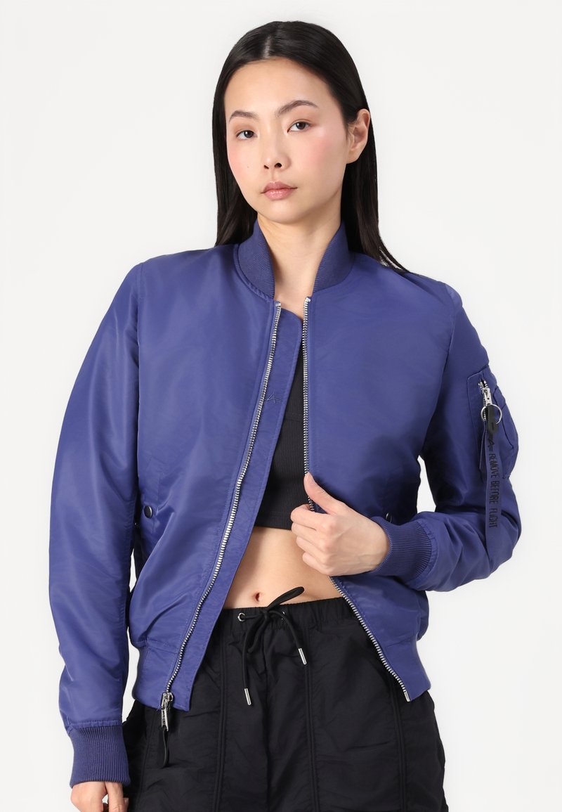 Purple bomber jacket with a zip front, ribbed cuffs, and side pockets. Features a zippered arm pocket and a smooth, glossy texture.