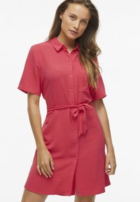 Ružové šaty so zapínaním na gombíky, s opaskom v páse, krátkymi rukávmi a textúrovanou látkou. Obsahujú golier a náprsní vrecko.
