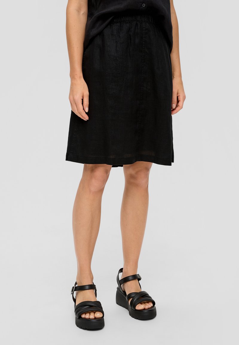 Jupe en lin noir avec une taille élastique, longueur genou, dotée d'une texture lisse. Assortie à des sandales à plateforme noires à lanières.