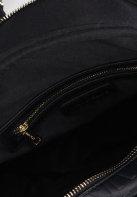 Zwart handtas interieur met een gladde stofvoering, een goudkleurige rits en een leren pocket met textuur.