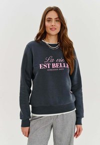 Tmavohnedá mikina vyrobená z mäkkého materiálu, s ružovým nápisom "La vie EST BELLE SUNKISSED DAYS." Pružné manžety a spodný lem, voľný strih.