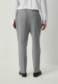Pantalones gris claro hechos de tejido texturizado, con corte recto, passadores para cinturón y dos bolsillos traseros. Llevados con zapatos negros.