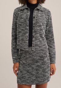 Svart och vit tweedjacka och kjolsats med kragsdesign, med knäppningar och en strukturerad tyg. Slät, figurnära passform.