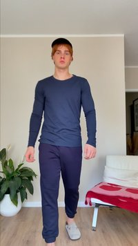 Cămașă albastră cu mânecă lungă și pantaloni de trening negri, cu papuci gri. Fundalul prezintă un ghiveci alb și un scaun crem cu o pătură roșie.