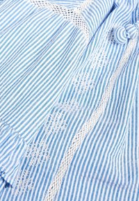 Vaaleansininen ja valkoinen raidallinen kangas, jossa on brodeerattu kukkakuvio. Omistaa pitsiyksityiskohtia saumoissa, pehmeän pinnan ja kevyen muotoilun.