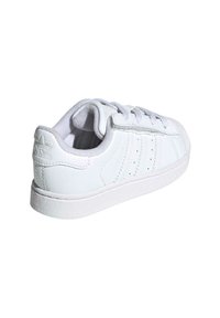 White leather sneaker with textured accents, round toe, three side stripes, and lace-up design. Smooth sole and padded collar for comfort.