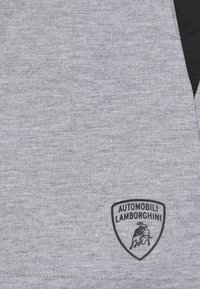 Tejido gris con detalle triangular negro y pequeño logotipo negro de Automobili Lamborghini que presenta el emblema de un toro en carga.