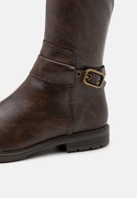 Bottine en cuir marron avec une boucle décorative en laiton et un talon bas solide sur fond blanc.