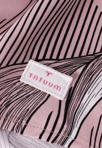Gros plan d'un tissu rose et noir à motifs avec une étiquette blanche portant la mention "TATUUM" en lettres roses cousue sur le tissu.
