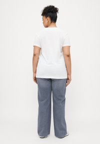 Tricou alb cu mânecă scurtă și guler rotund, asociat cu blugi largi de culoare albastră deschisă. Materialul pare moale și neted.