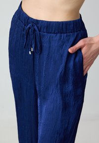 Marineblauwe, gekreukte stoffen broek met een elastische tailleband, verstelbare sluiting en zijzakken. Glad textuur, ontspannen pasvorm.