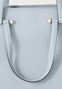 Borsa tote in pelle azzurra chiara con manici piatti, caratterizzata da dettagli in hardware dorato e cuciture visibili. Texture liscia, forma rettangolare.