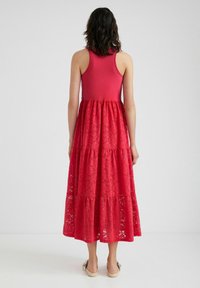 Röd maxiklänning med en figurnära ärmlös topp och en lager-på-lager spettskjorta. Texturerad spettsbygd med ett dekorativt blommönster.