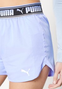 Vaaleanvioletit shortsit, joissa on musta joustava vyötärönauha, jossa lukee 'PUMA'. Sivuhalkiot tarjoavat ilmanvaihtoa, ja vasemmassa lahkeessa on valkoinen logo.