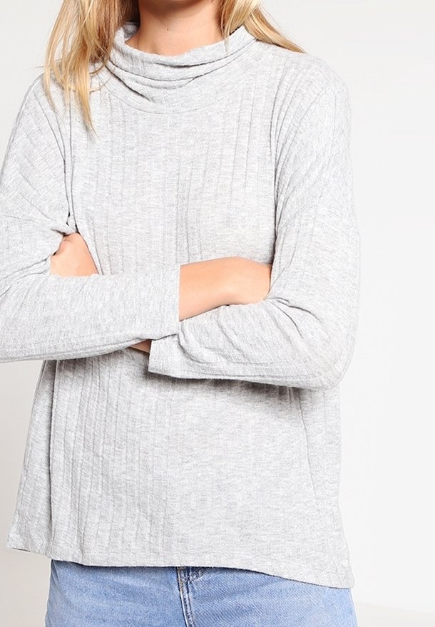 Vaaleanharmaa, ribattua pitkähihaista paitaa, jossa on kaula-aukko, rento mitoitus ja sivuhaalareita, yhdistettynä sinisiin farkkuihin. Pehmeä rakenne.