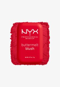 Stick blush Buttermelt rouge de NYX Professional Makeup sur fond de poudre rouge écrasée sur une surface blanche.