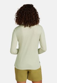 Camicia a maniche lunghe verde chiaro realizzata in un tessuto liscio e texture, abbinata a pantaloni corti khaki, vista da dietro.