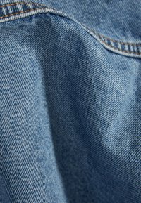 Jeansmaterial i ljusblått, med en texturerad väv och synliga stygn längs kanterna. Slät och något skrynklig utseende.